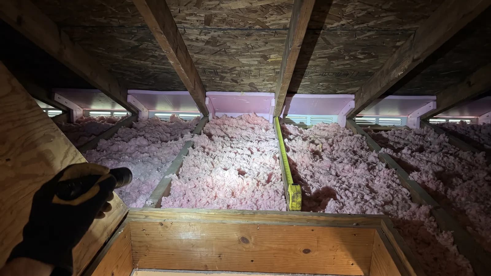 Flashlight on attic insulation and soffit vent baffles between the rafters