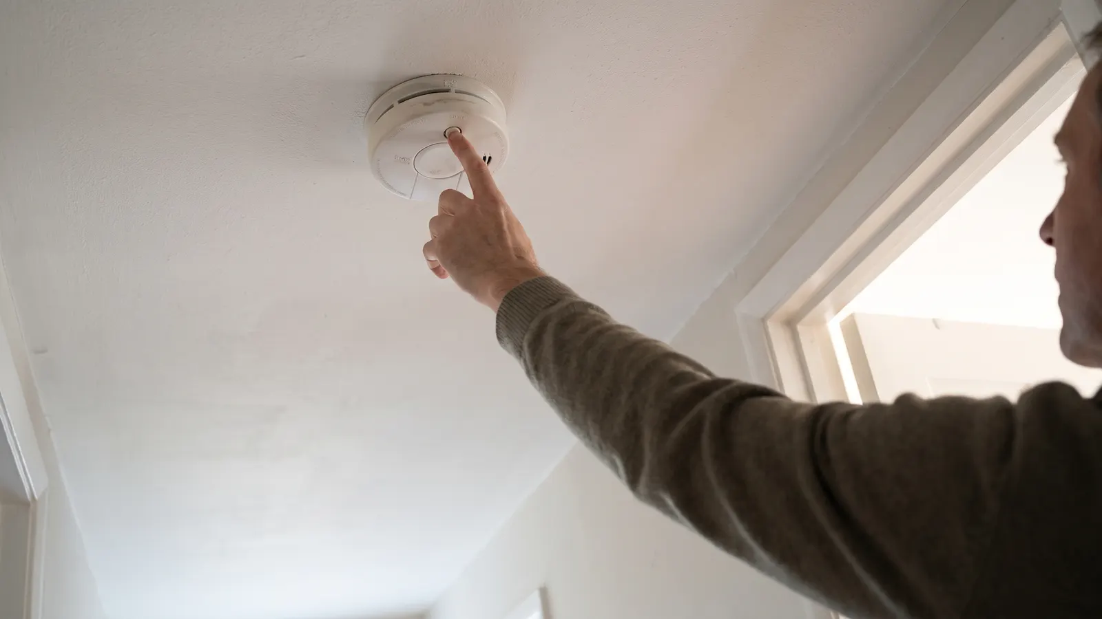 Pressing the test button on a ceiling smoke and carbon monoxide alarm